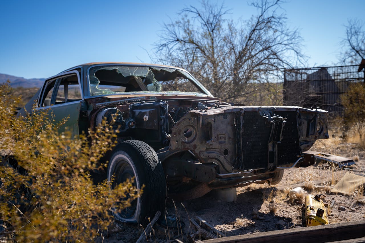 A decaying car in the Arizona desert surrounded by dry plants and a clear blue sky.